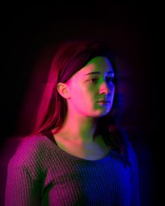 Young woman looking forward bathed in coloured light and shadow