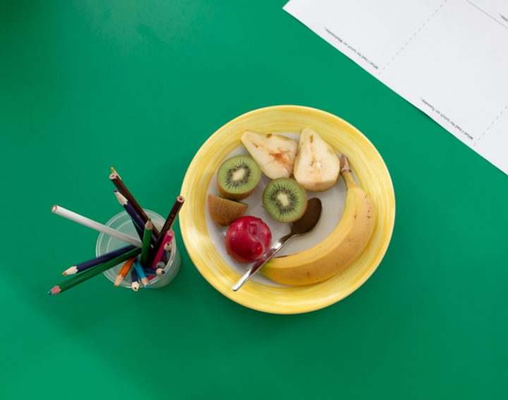 a plate of mixed fruit with a pot full of pencils and pens on a school desk