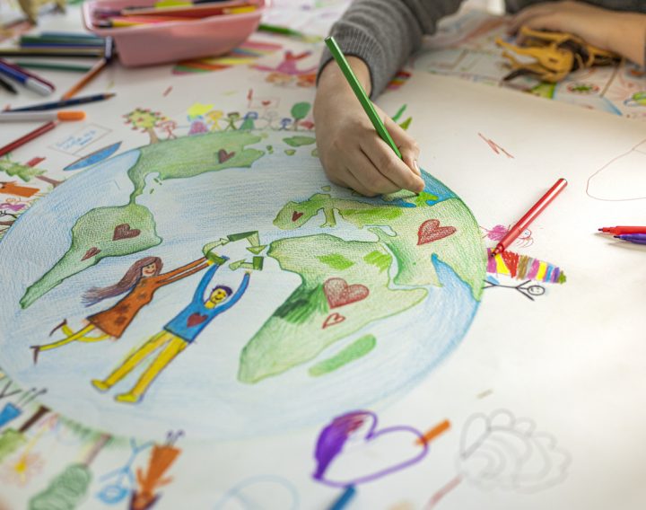 a photograph of children's hands drawing a picture of the planet and people linking hands around it