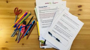 A pile of application forms for Young Start funding on a desk with pens and pencils