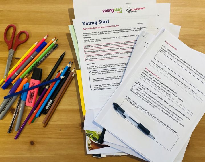 A pile of application forms for Young Start funding on a desk with pens and pencils