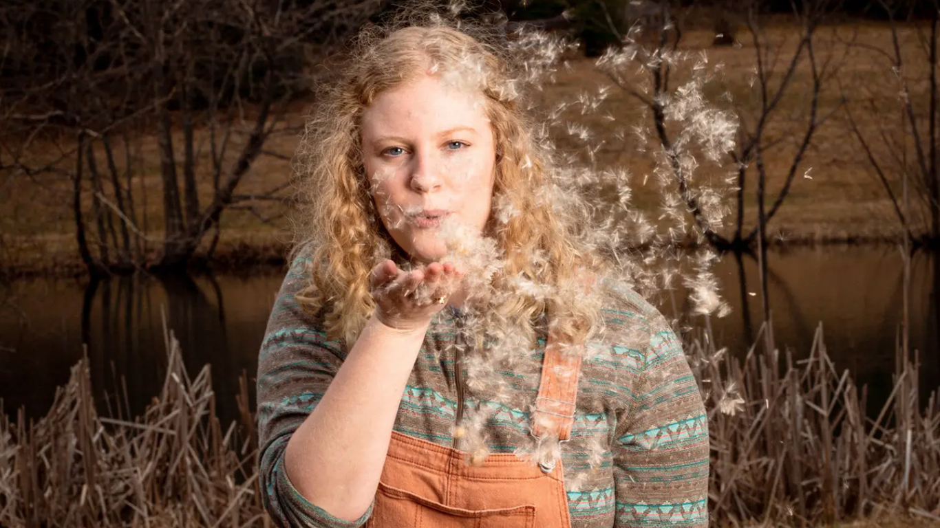 a photo of a young woman blowing dandelion seeds from her hand