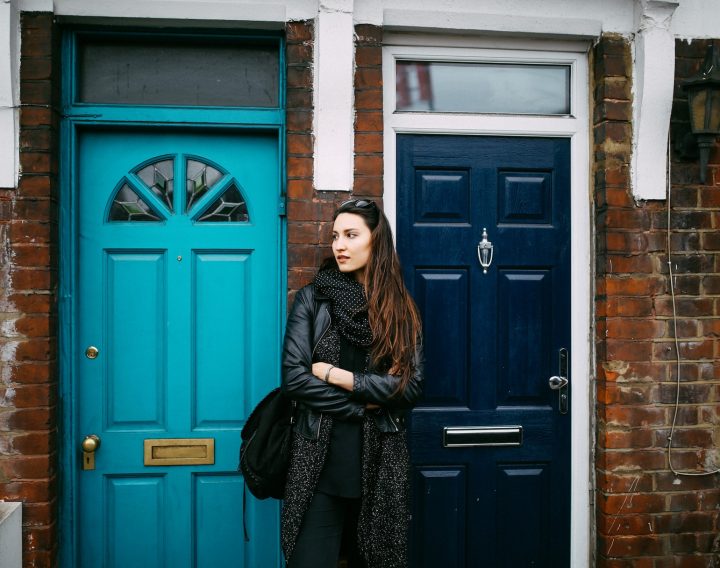 A young woman stood between two front doors, looking unsure.